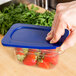 A hand using a blue Carlisle Smart Lid to cover a plastic container of strawberries.