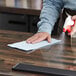 A hand using a blue WypAll heavy-duty foodservice wiper to clean a counter.