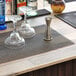 A Tablecraft black plastic mesh bar mat on a counter with glasses and a bottle.