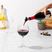 A person using an OXO wine pourer to pour red wine into a glass.