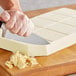 A person cutting a Callebaut white chocolate block with a knife.