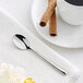 An Acopa stainless steel demitasse spoon on a white napkin next to a cup of coffee.