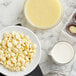 A bowl of Callebaut white chocolate chips on a marble counter near a bowl of milk.