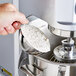 A hand using a Vollrath stainless steel transfer bowl to measure flour.