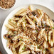 A white plate with pasta, mushrooms, and sunflower seeds.