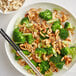 A bowl of food with broccoli and cashews with chopsticks.