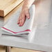 A hand holding a red-striped herringbone kitchen towel over a counter.