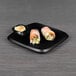 An Elite Global Solutions black melamine chip and dip plate with sushi rolls and dipping sauce on it.