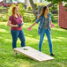 Two women playing the Backyard Pro Courtyard birchwood cornhole set on grass.