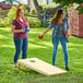 Two women playing Backyard Pro wood cornhole in a yard.