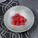 A Denali cement embossed melamine bowl filled with raspberries on a table.