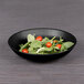 A matte black Elite Global Solutions melamine bowl filled with salad and tomatoes.