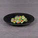 A matte black Elite Global Solutions Hermosa Melamine Plate with salad on it.