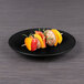 An Elite Global Solutions matte black melamine plate with skewers of vegetables on it on a table.