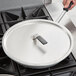 A person using a Vollrath Torogard pot lid to cover a pan on a stove.