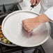 A person using a Vollrath aluminum pan with a Torogard handle to prepare food.