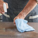 A hand using a blue Unger MicroWipe Pro cloth to clean a table