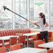 A woman using an Unger Stingray extension pole to clean a restaurant table.