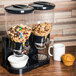 A Zevro double dry food dispenser with cereal and a muffin on a table.