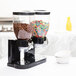 A black Zevro double dry food dispenser on a table with cereal and chocolate in it.