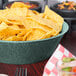A large round polyethylene basket filled with tortilla chips on a table.