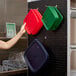 A woman using a green plastic container on a black Camshelving® pegboard to hold a group of plastic containers.