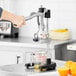A hand using the Choice Prep Manual Citrus Juicer to juice half an orange over a measuring cup.