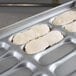 A tray of hot dog bun dough on a Chicago Metallic hot dog bun pan on a counter.
