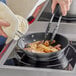 A person cooking food in a Vollrath stainless steel pan on a stove.