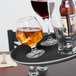 A Carlisle black non-skid serving tray with wine glasses and a bottle on it.