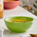 An Acopa Capri green stoneware bowl filled with soup with a spoon next to it.