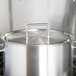 A large silver stainless steel pot lid with a loop handle over a pot.