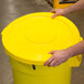 A hand placing a Continental Huskee yellow lid on a yellow trash can.