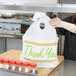 A woman holding a white plastic LK Packaging take out bag with a printed thank you design.