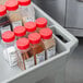 A Continental gray utility cart with a recessed top holding plastic containers and bottles with red caps full of spices.