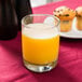 An Anchor Hocking Room Tumbler filled with orange juice on a table with muffins.
