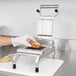 A person in gloves using a Nemco Easy Chicken Slicer to cut a piece of meat.