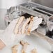 A person in gloves using a Nemco Easy Chicken Slicer to cut chicken on a counter.
