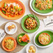A table with plates of food and Acopa Valencia Orange stoneware bistro bowls filled with noodles and vegetables.