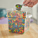 A close up of a person using a Vigor clear plastic container to pour candy into a bowl.