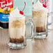 A glass mug of brown liquid with white foam and a straw next to a bottle of Torani Root Beer Flavoring Syrup.
