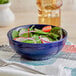 An Acopa Capri deep sea cobalt stoneware bowl filled with salad and vegetables on a table in a salad bar.