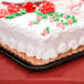 A white cake with red and green flowers on a gold laminated rectangular cake pad.