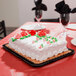 A rectangular gold laminated cake pad with a white cake decorated with red and green frosting on a table.