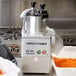 A Robot Coupe CL50 Gourmet food processor with shredded carrots in a white container.