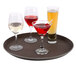 A Thunder Group brown non-skid serving tray holding three glasses of wine, including red and white.