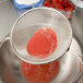 A Tablecraft double mesh strainer removing red liquid from a bowl.