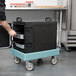A person using a Cambro Slate Blue Camdolly to transport a Cambro Camtainer.