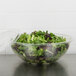 A Sabert clear PET round bowl filled with green and red lettuce on a counter.