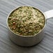 A metal measuring cup filled with Regal Herbs and Garlic Blend.